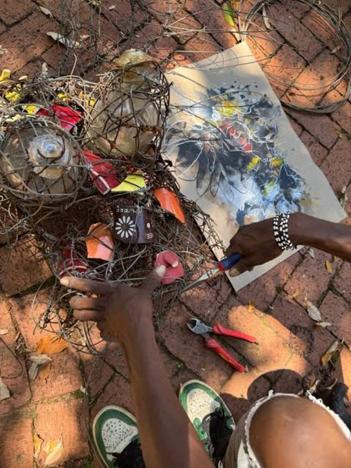 Hands twisting wire with pliers beside a working drawing on a brick courtyard